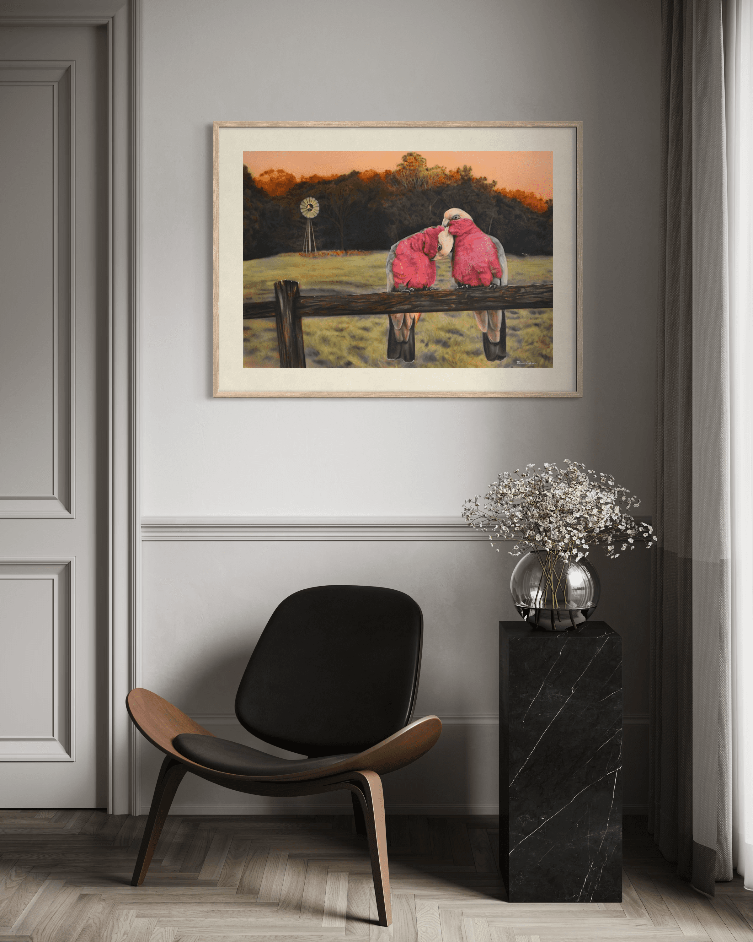 Framed painting of pink galahs on a fence above a black chair and marble pedestal.