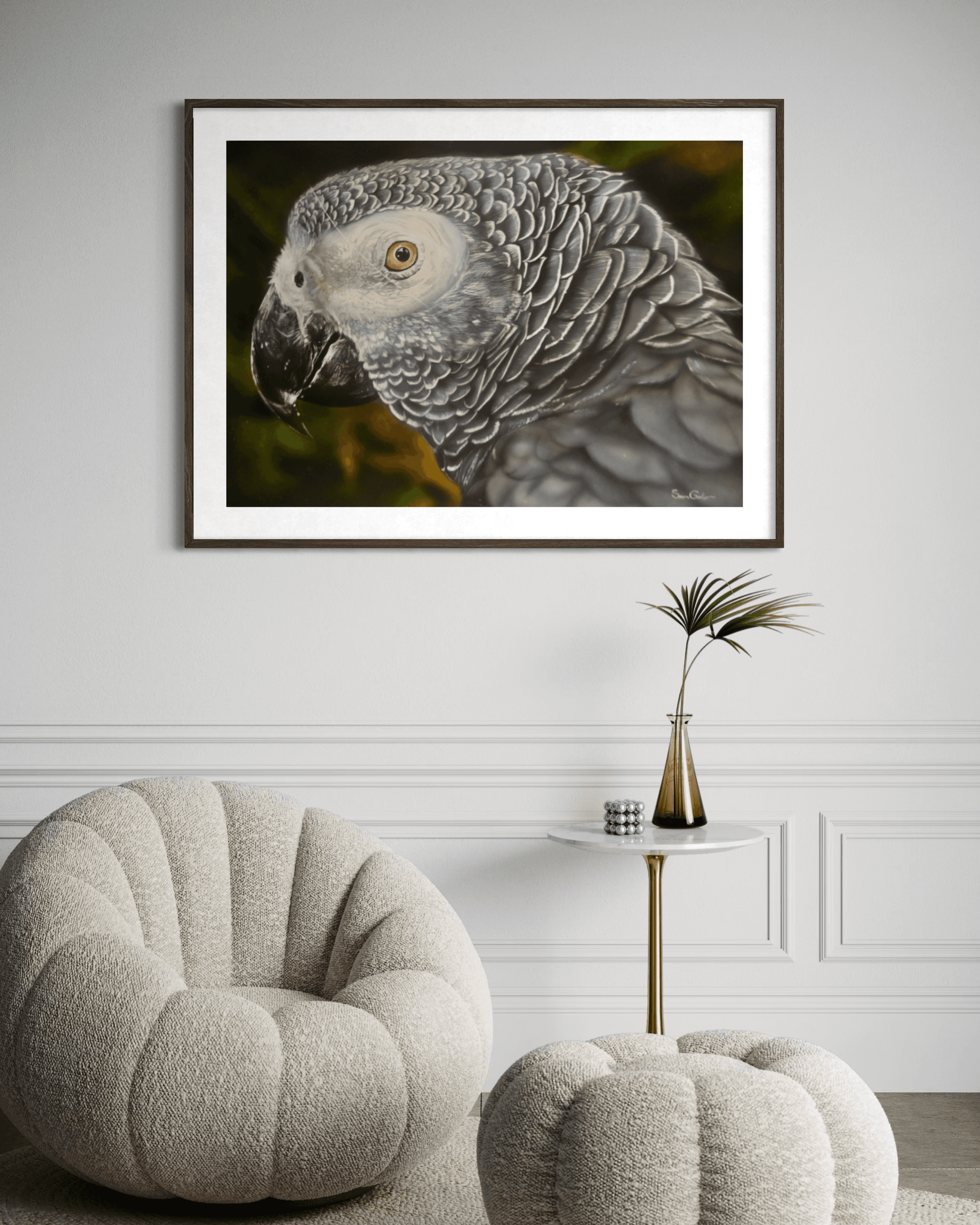 Framed African Grey Parrot portrait hanging on a white wall above a textured cream armchair.