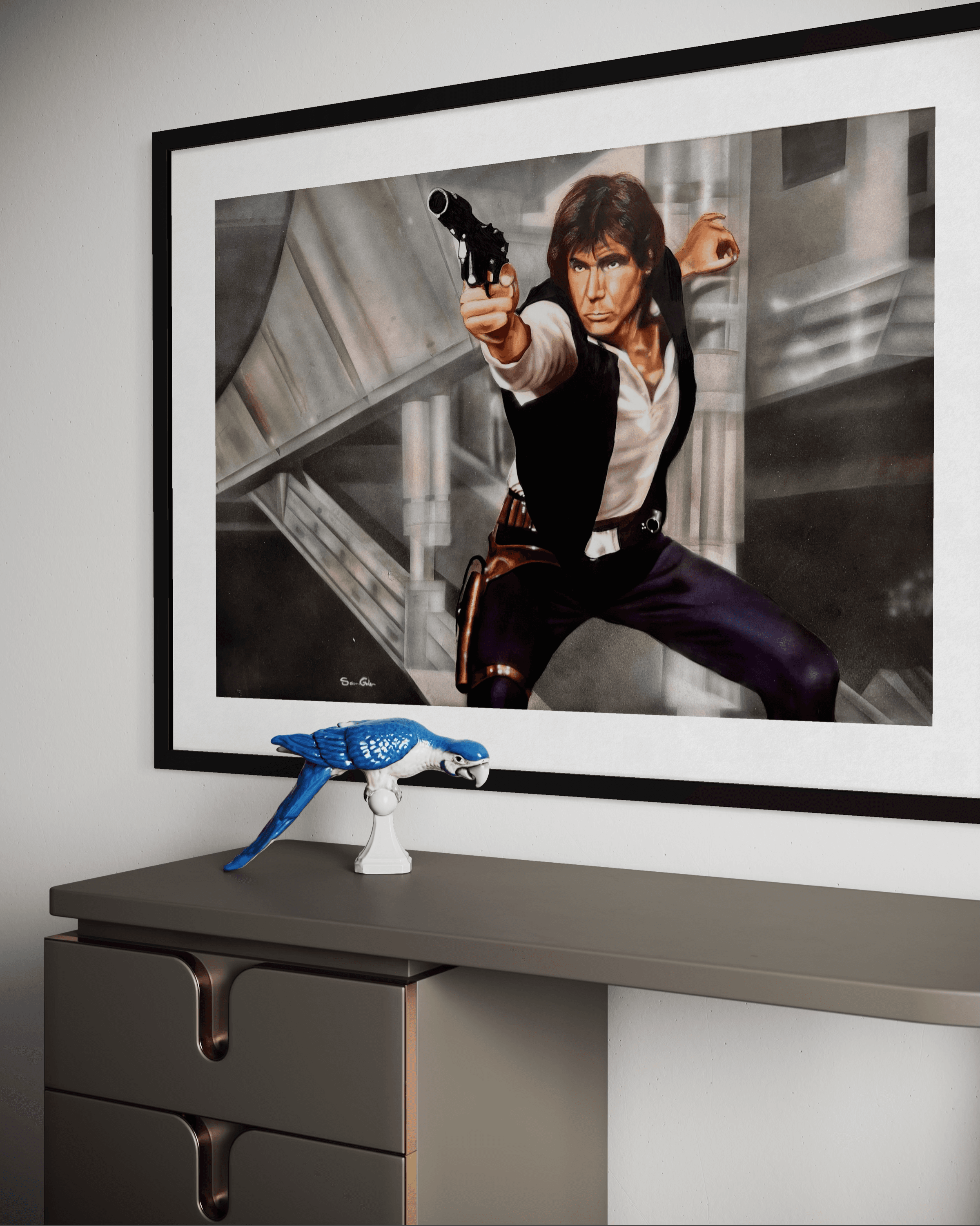 Framed Han Solo painting pointing a blaster above a desk with a blue parrot figurine.